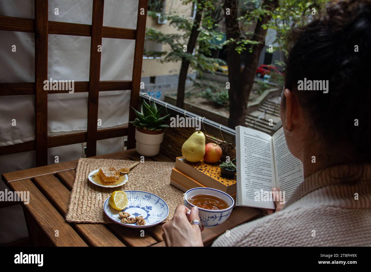 Picture from back of young woman enjoying quiet morning time at balcony, having a tea with organic honey and few fruits from organic farm Stock Photo