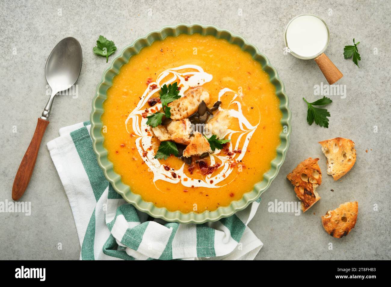 Pumpkin and carrot cream soup with herbs, seasonings and seeds in bowl on gray concrete table background in rustic style. Thanksgiving traditional aut Stock Photo