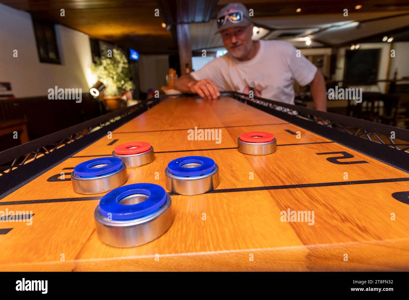An intense game of shuffleboard captures a man in casual attire