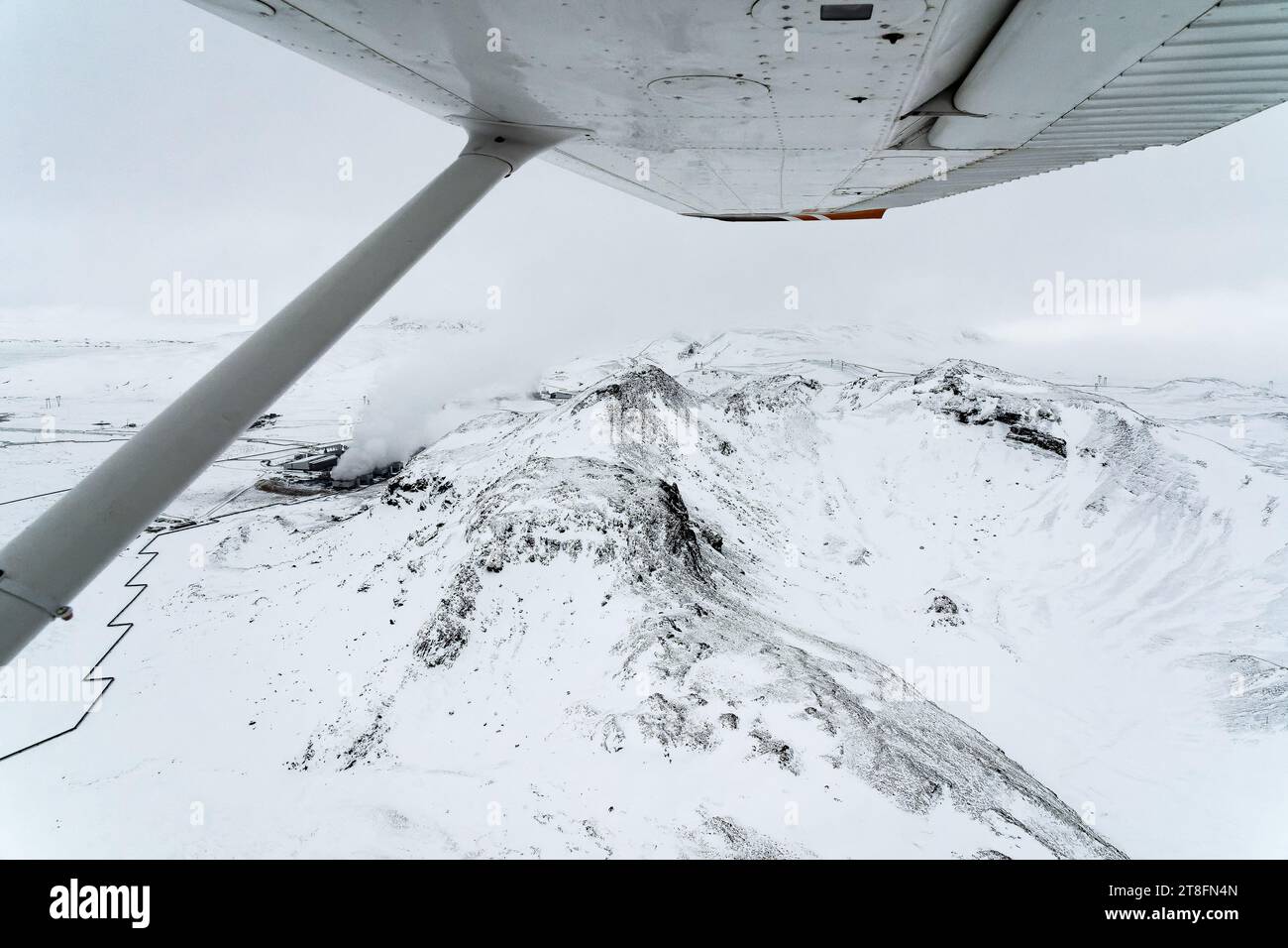 Aerial view of rugged snow-covered mountains stretching into the horizon, captured from the underbelly of a small aircraft Stock Photo