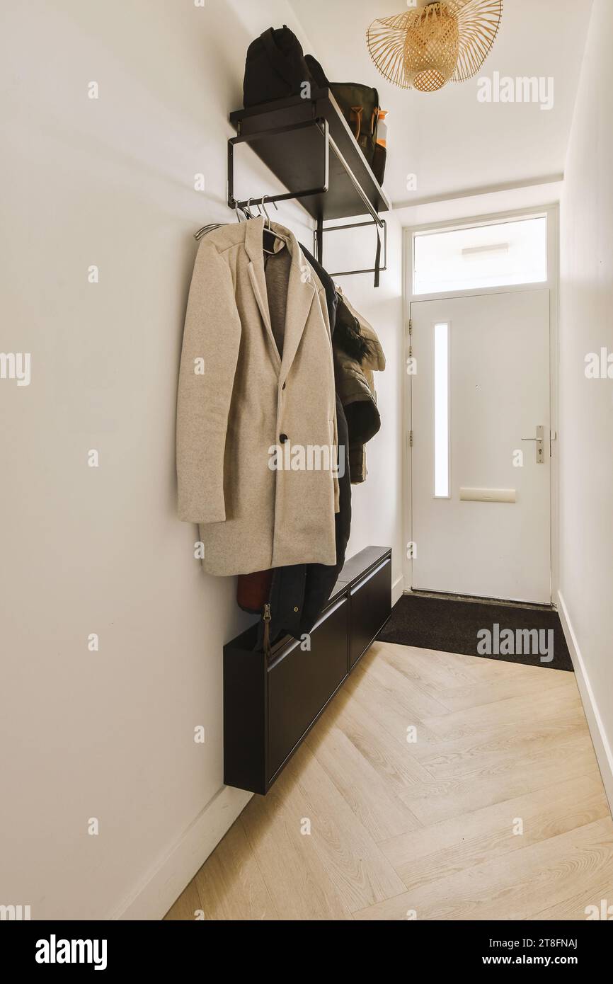 Interior of hallway with coats hanging on rack and closed door at contemporary house with white walls and parquet floor Stock Photo