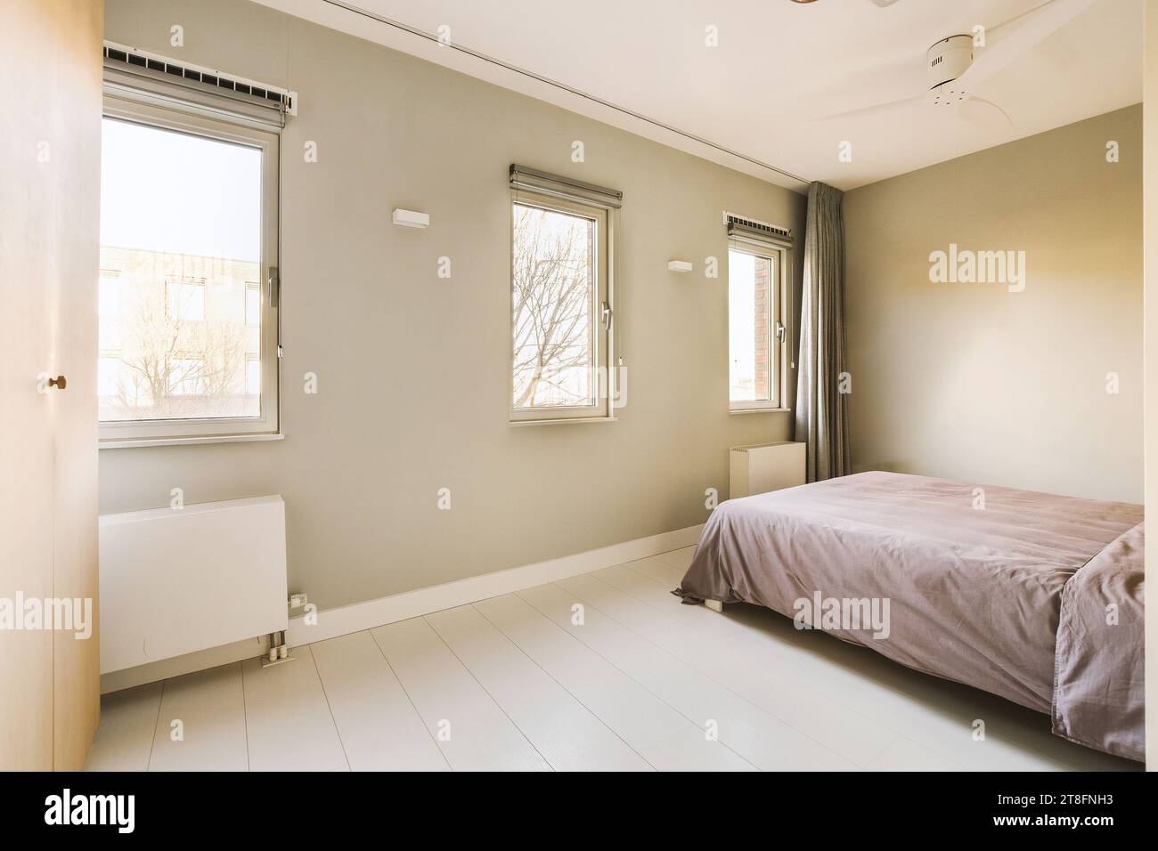 Interior of spacious bedroom with comfortable bed and bright windows in modern house with grey walls Stock Photo