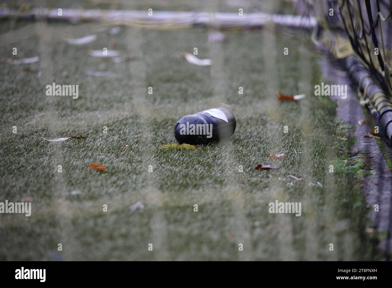 An empty, clear glass soda bottle on the ground in front of a white picket fence Stock Photo