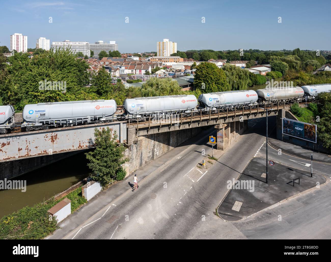 A freight train of tanker wagons crosses Feeder Road and the Feeder Canal in the industrial St Philip's Marsh area of Bristol, with the Barton Hill ne Stock Photo