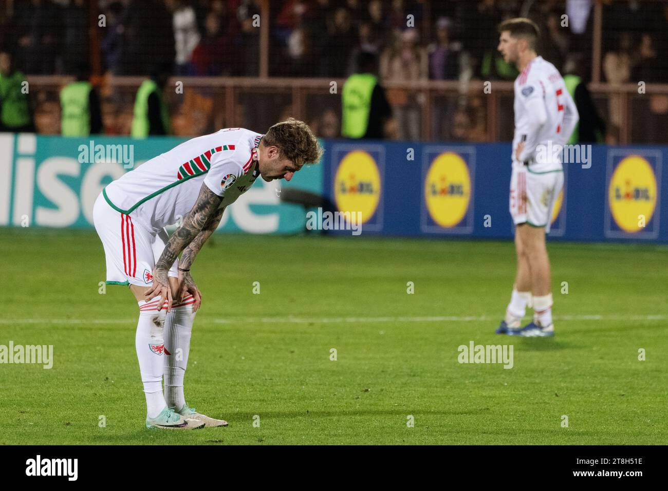 A young adult soccer player in a white and blue uniform is dejectedly crouching on the field, resting their head in their hands Stock Photo