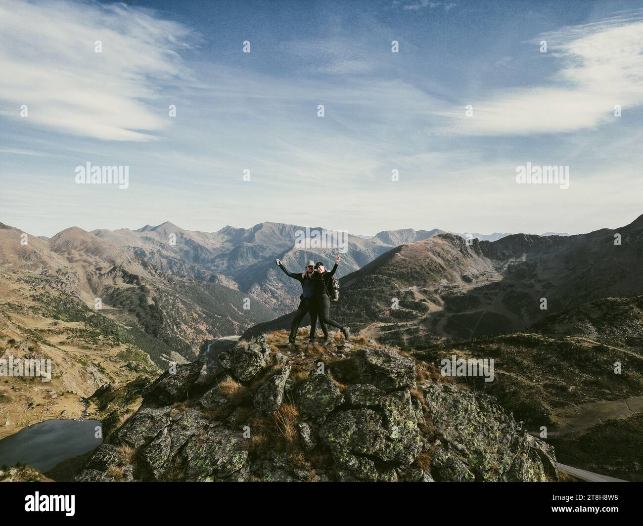 A man and a woman stand atop a mountain peak, looking out over the vast ...