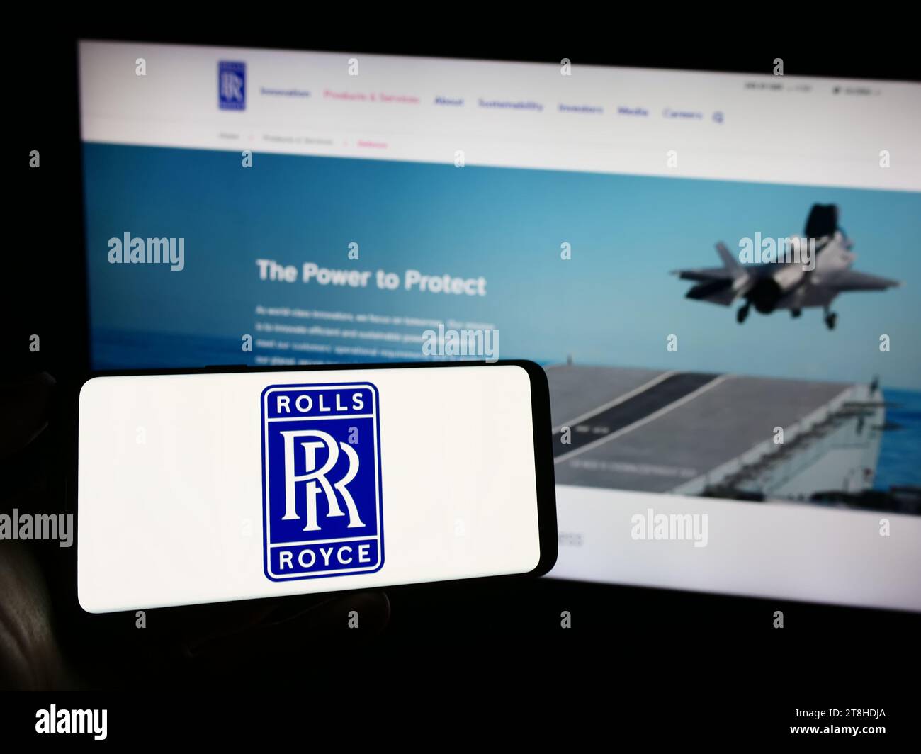 Person holding mobile phone with logo of British aerospace company Rolls-Royce Holdings plc in front of web page. Focus on phone display. Stock Photo