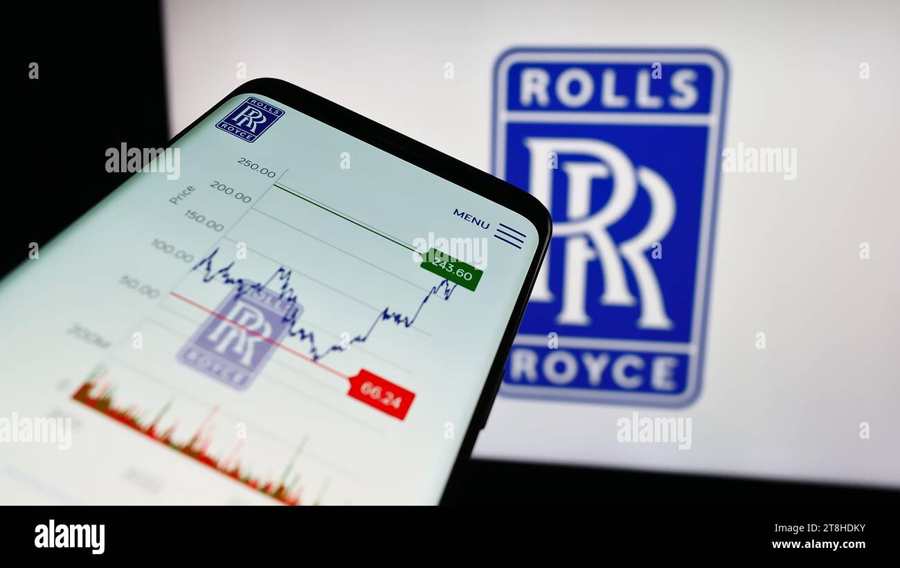 Mobile phone with website of British aerospace company Rolls-Royce Holdings plc in front of business logo. Focus on top-left of phone display. Stock Photo