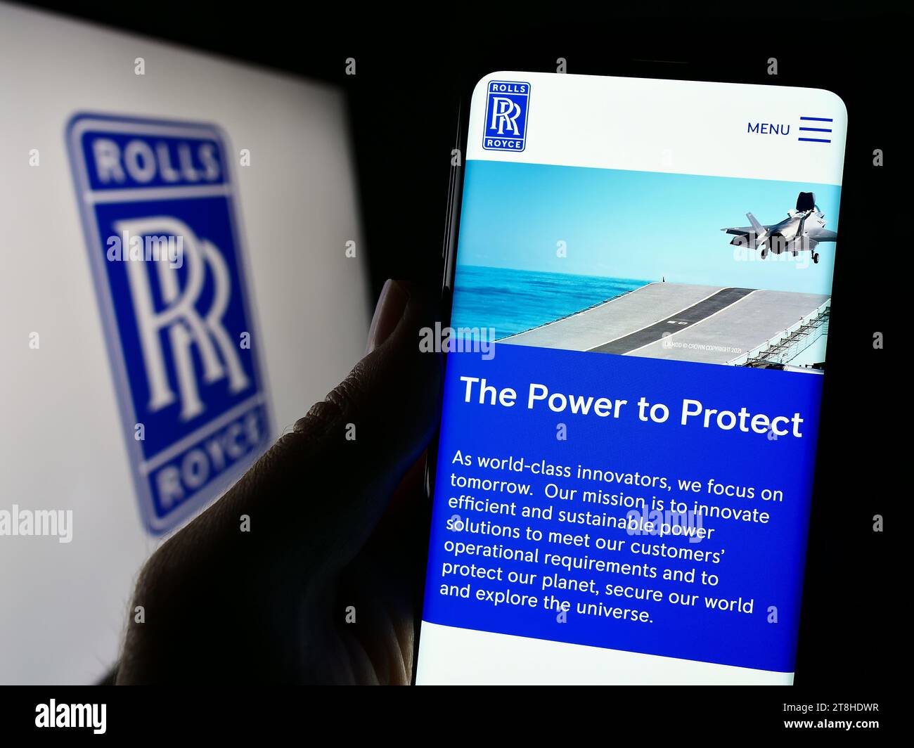 Person holding smartphone with website of British aerospace company Rolls-Royce Holdings plc in front of logo. Focus on center of phone display. Stock Photo
