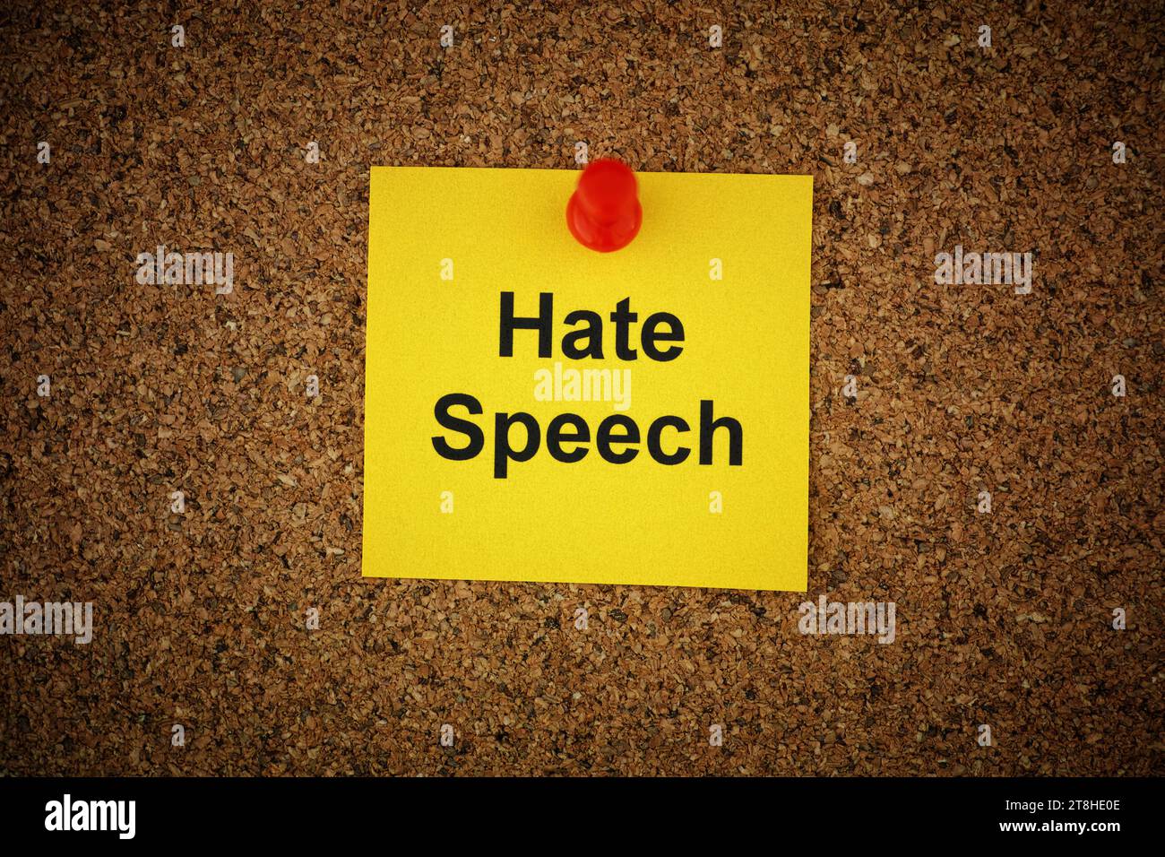 A yellow paper note with the words Hate Speech on it pinned to a cork board. Close up. Stock Photo