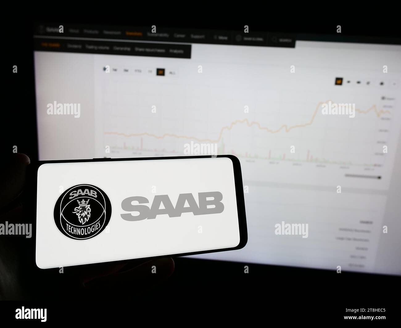 Person holding mobile phone with logo of Swedish aerospace and defense company Saab AB in front of business web page. Focus on phone display. Stock Photo