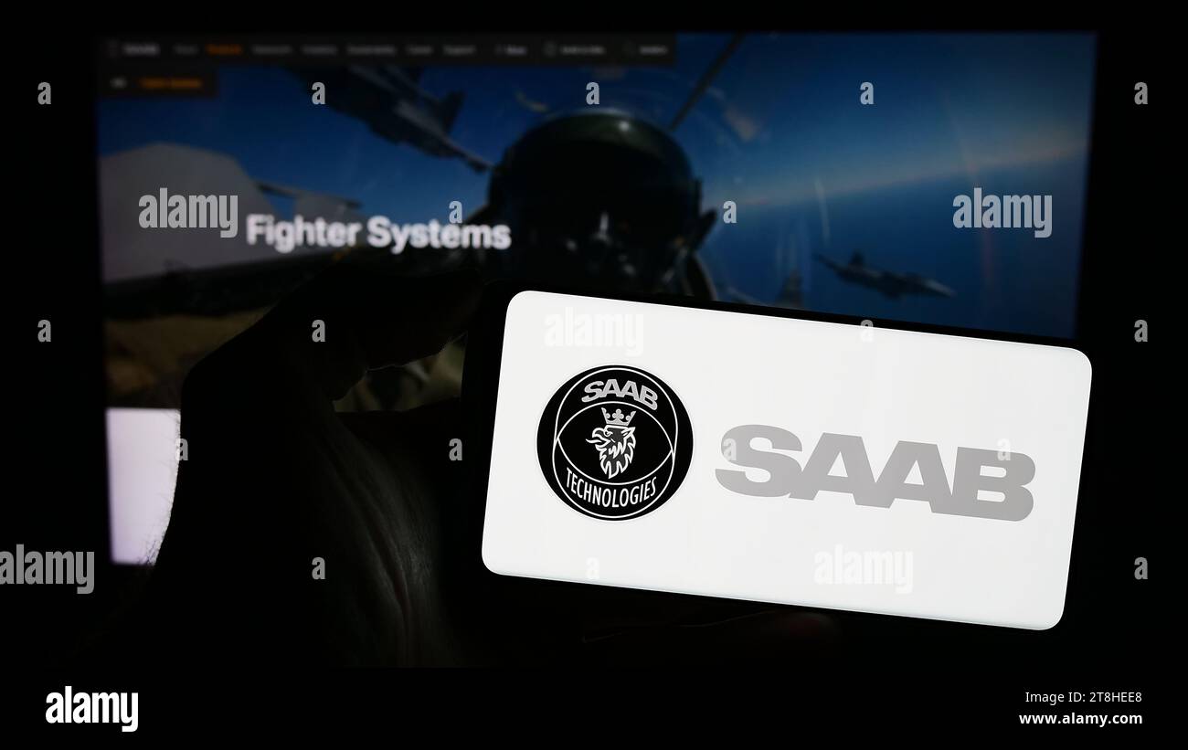 Person holding smartphone with logo of Swedish aerospace and defense company Saab AB in front of website. Focus on phone display. Stock Photo