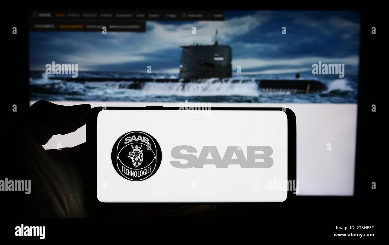 Person holding cellphone with logo of Swedish aerospace and defense company Saab AB in front of business webpage. Focus on phone display. Stock Photo