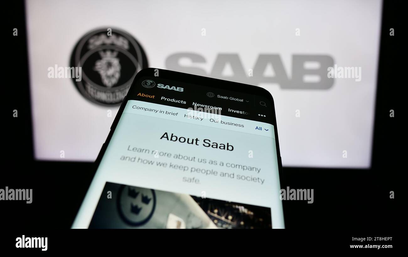 Mobile phone with webpage of Swedish aerospace and defense company Saab AB in front of business logo. Focus on top-left of phone display. Stock Photo
