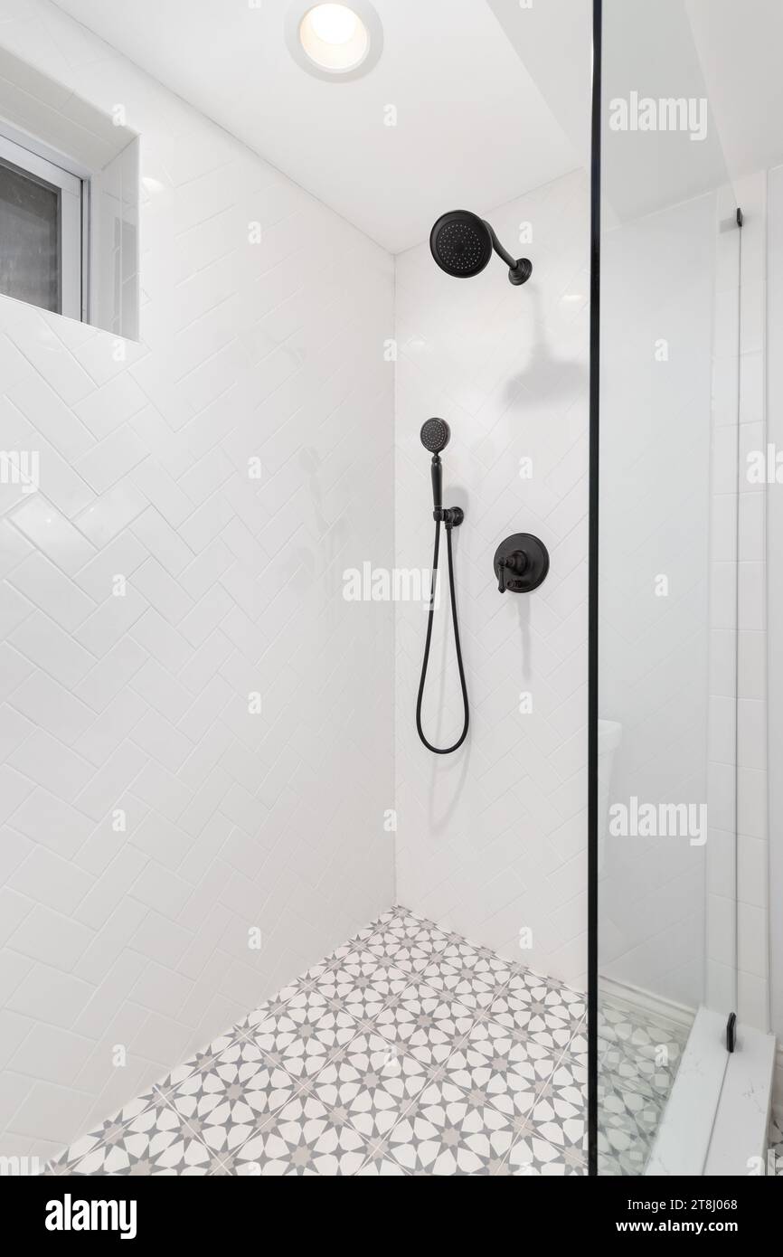 A bathroom shower with herringbone and mosaic tiles, a black showerhead