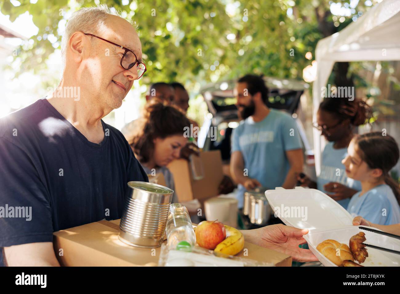 Detailed image of poor, needy caucasian man receiving meal box and canned goods from non-profit food drive. Close-up of low priviliged male individual getting free food from volunteers. Stock Photo