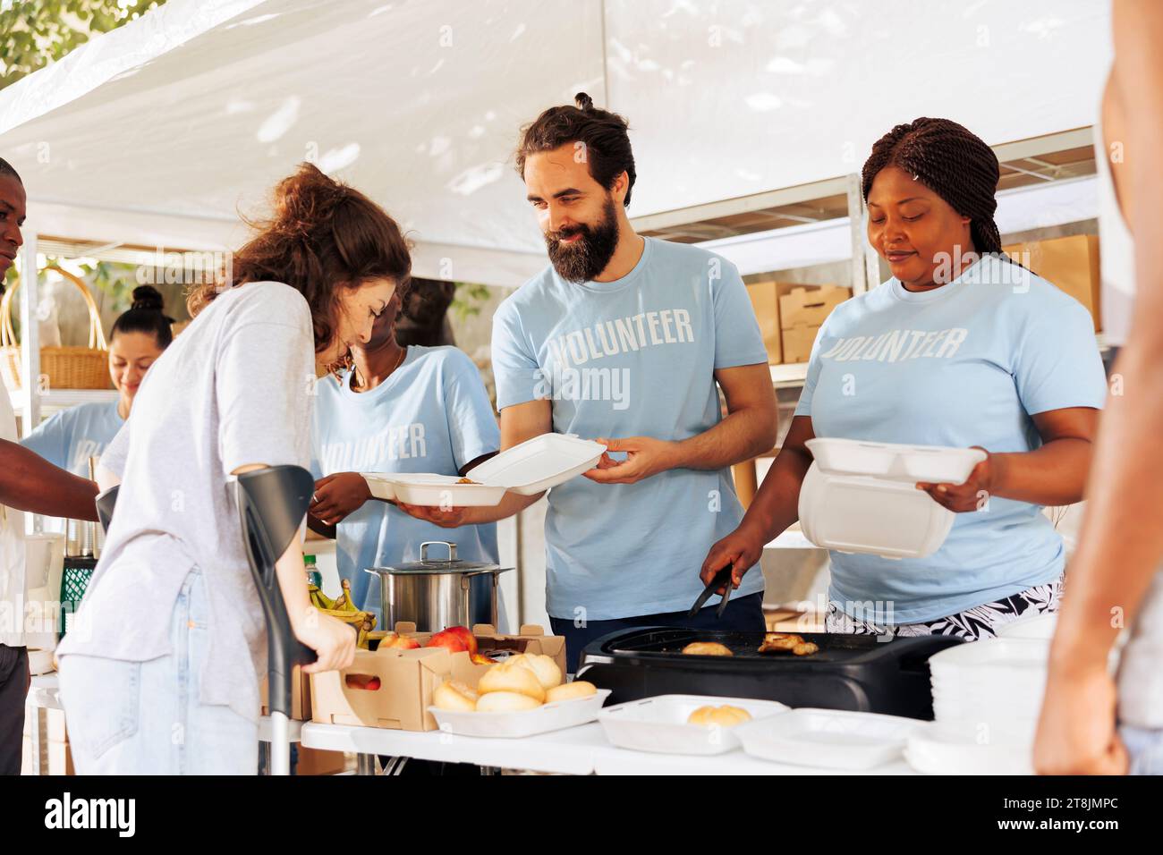Voluntary individuals helping disabled and homeless people with food and resources. Young people wearing blue t-shirt, display compassion by providing support to the needy and underprivileged. Stock Photo