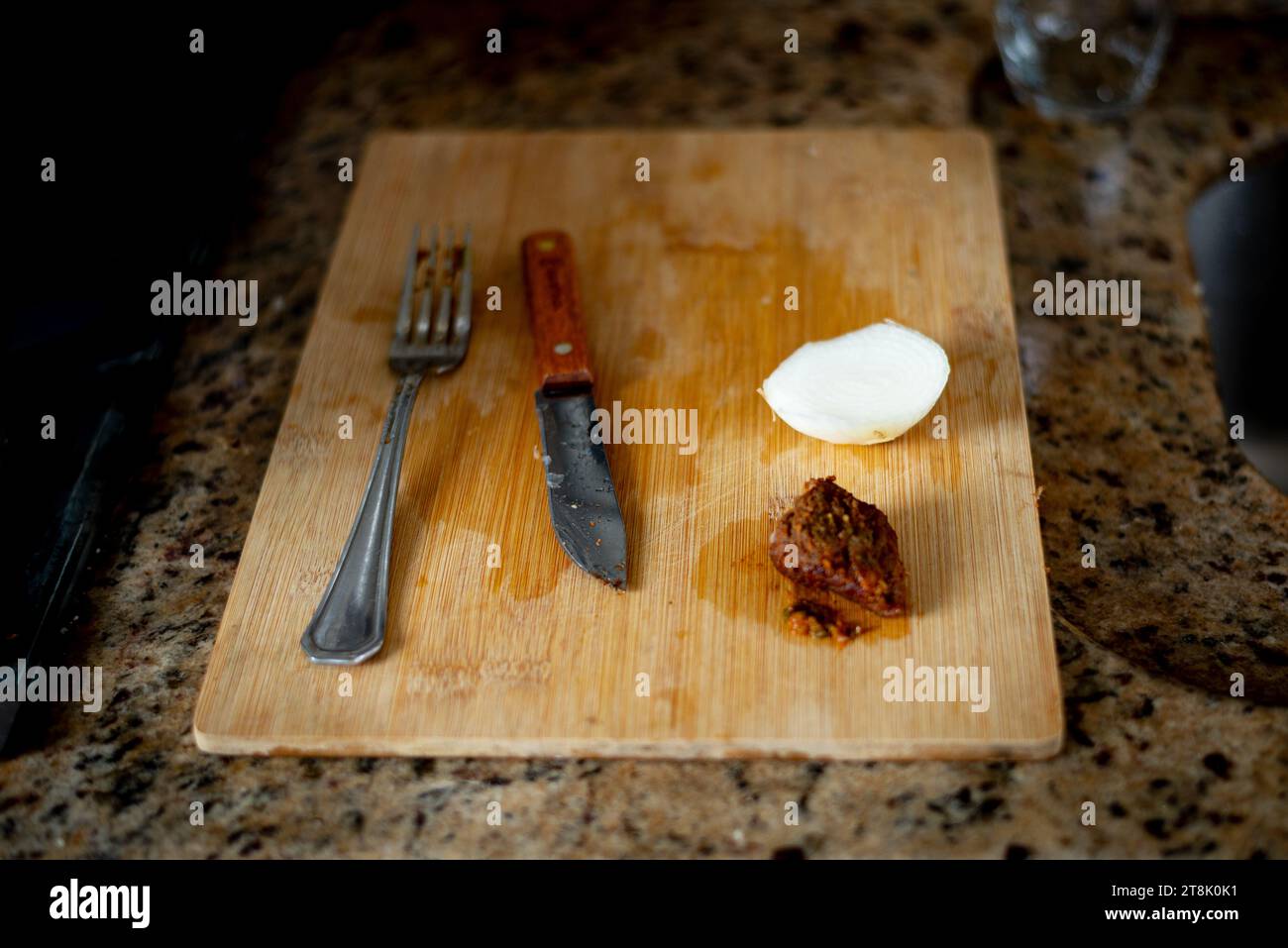 Wooden cutting board with knife, fork, meat and onion on top. Lunch preparation. Stock Photo