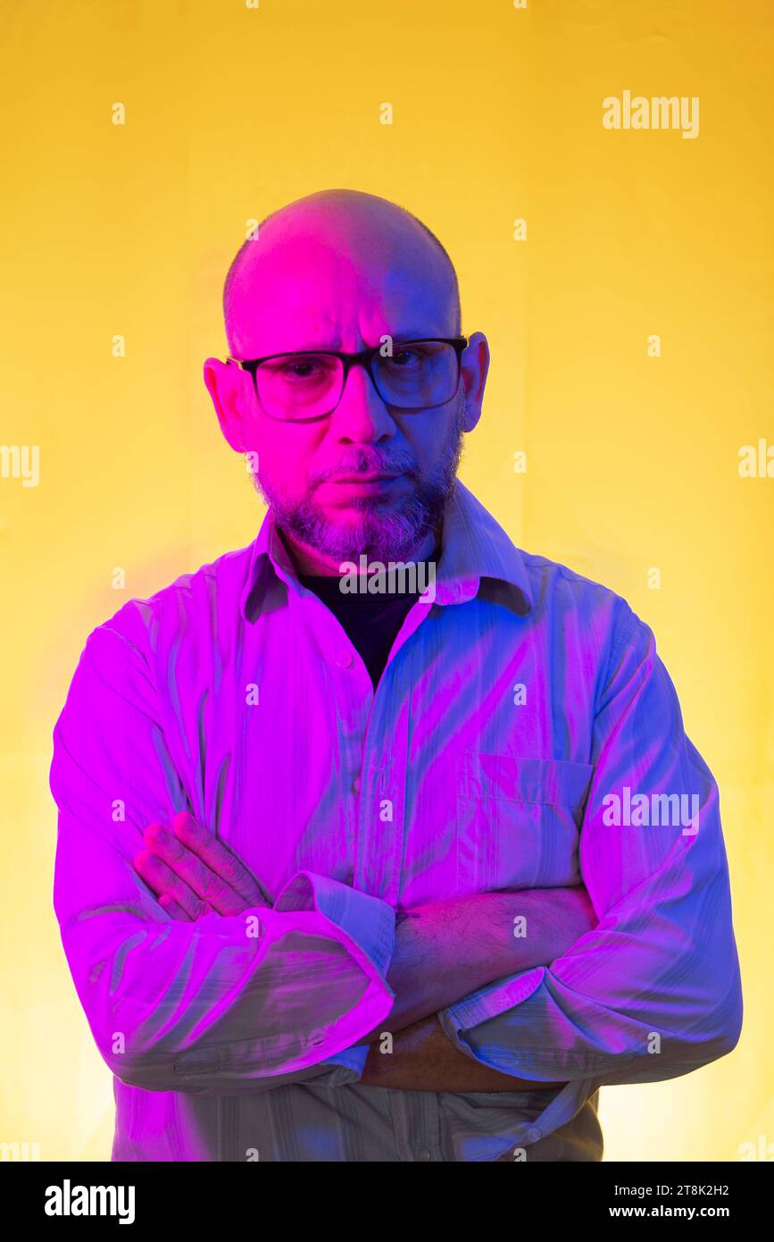 Bald, bearded man wearing prescription glasses against yellow background. Stock Photo