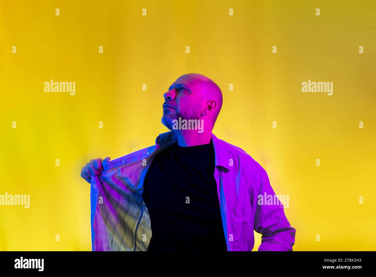 Bearded, bald man opening his shirt. Isolated on yellow background. Stock Photo