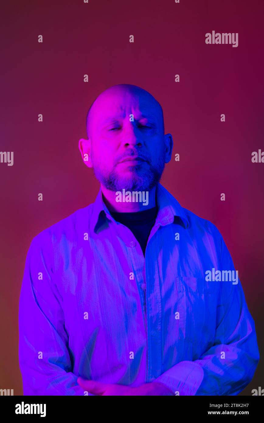 Bald, bearded man wearing business clothes against red background. Stock Photo