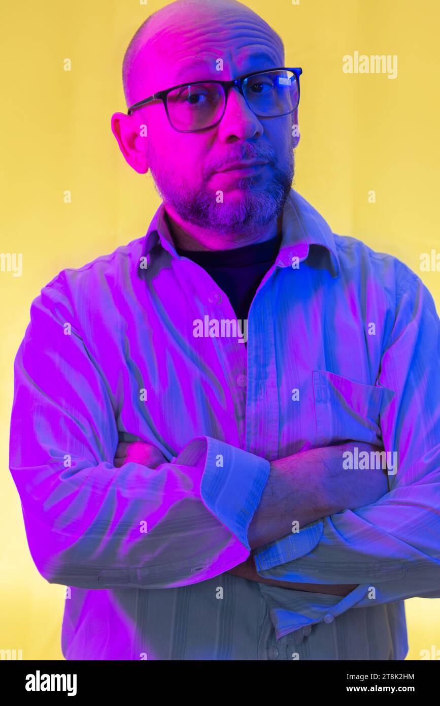 Bald, bearded man wearing prescription glasses against yellow background. Stock Photo