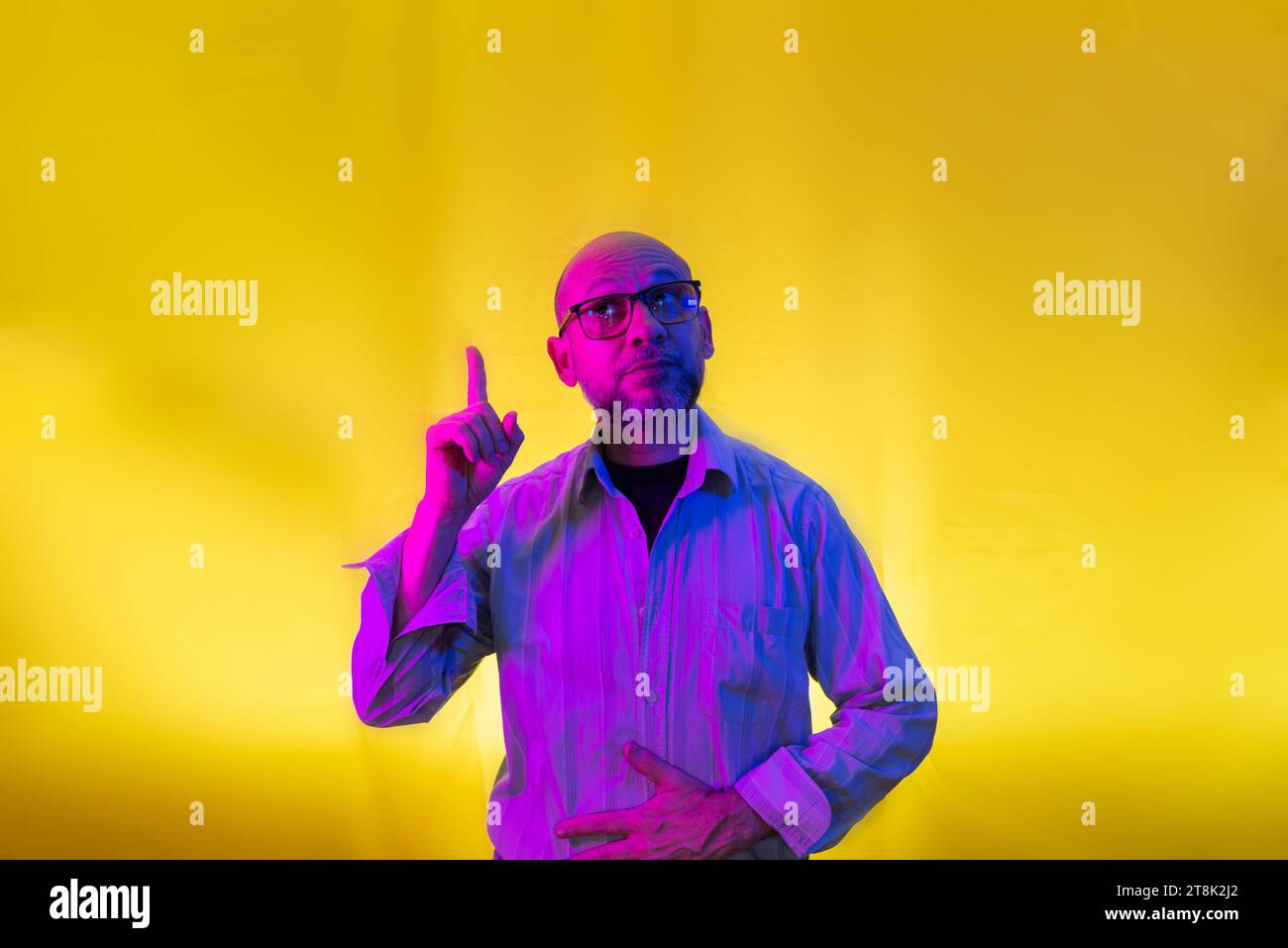 Bald, bearded man wearing glasses pointing up. Isolated on yellow background. Stock Photo