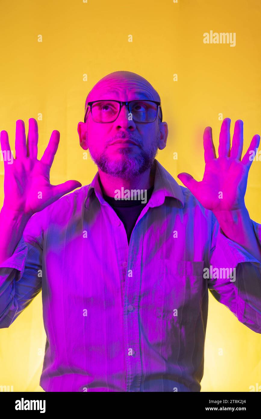 Bald, bearded man wearing glasses gesturing with his hands. Isolated on yellow background. Stock Photo