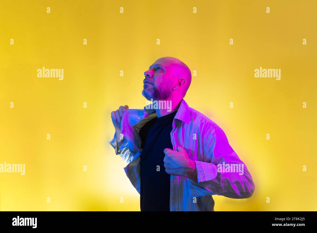Bearded, bald man opening his shirt. Isolated on yellow background. Stock Photo