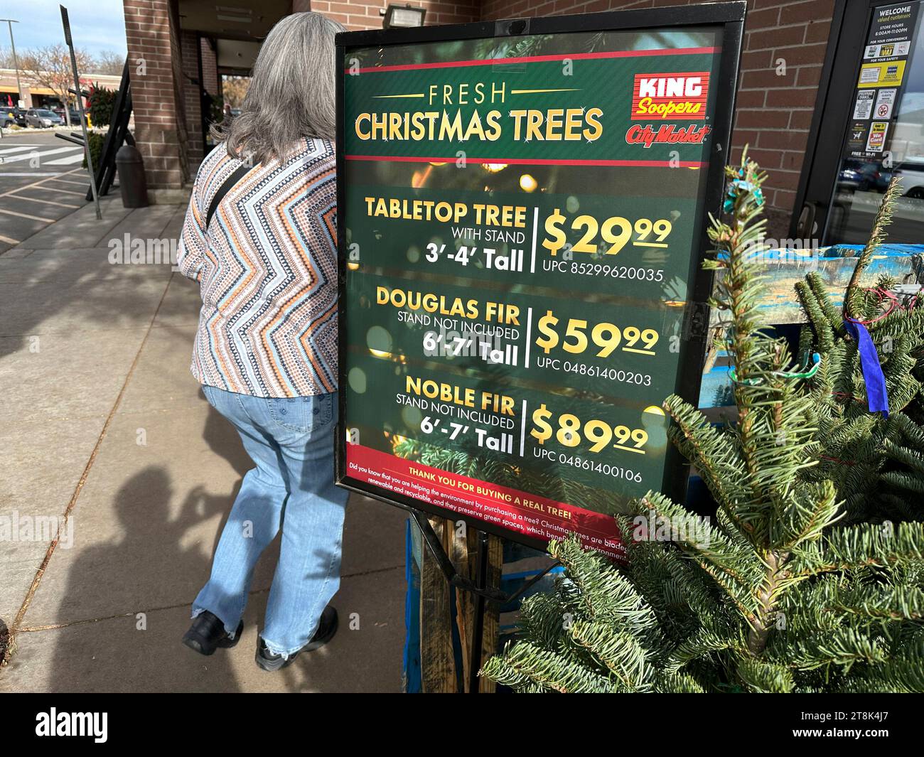 A shopper moves past a sign displaying the prices for various sizes of Christmas trees available