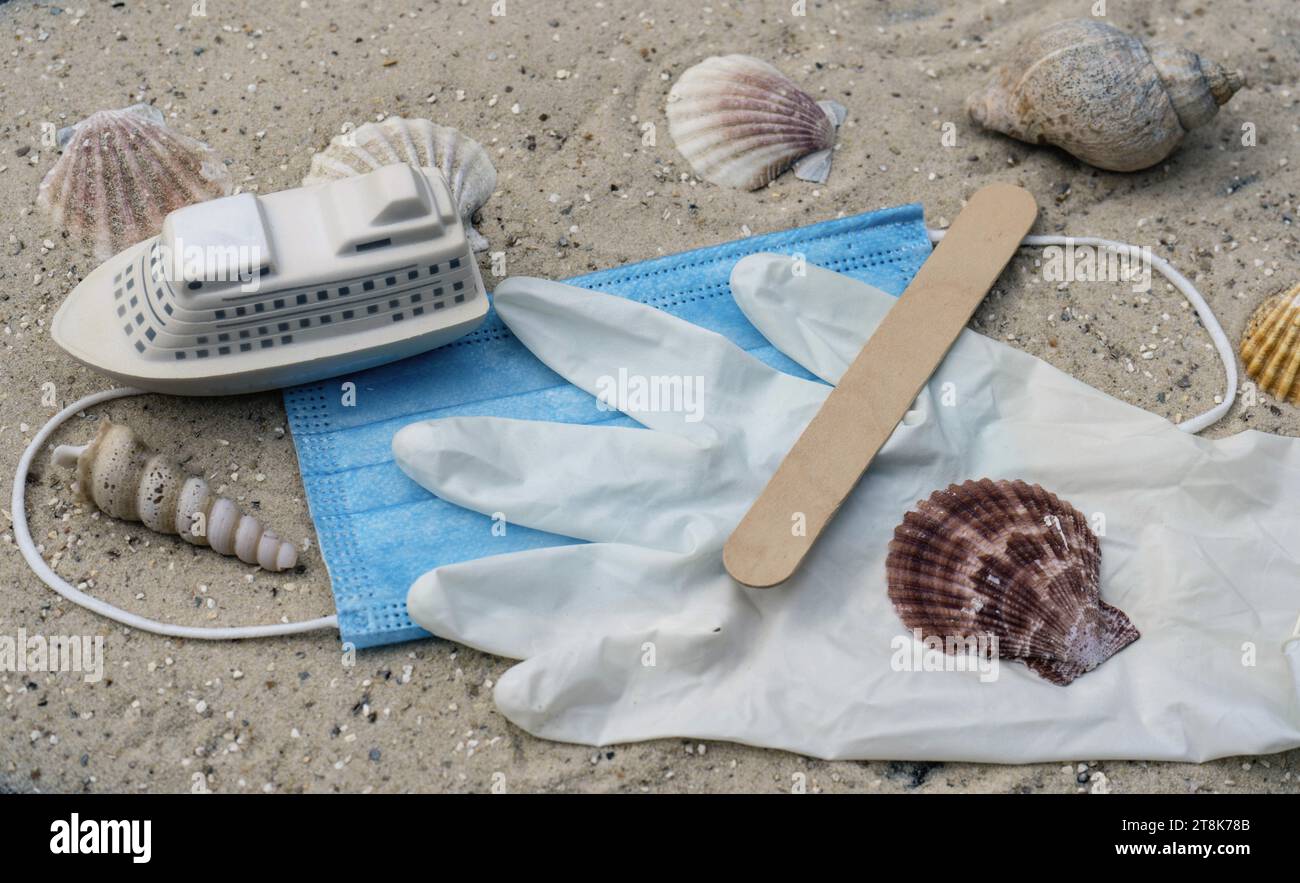 face mask, latex glove, spatula and ship, with shells and snailsshells on the beach, summer holidays under Corona conditions Stock Photo