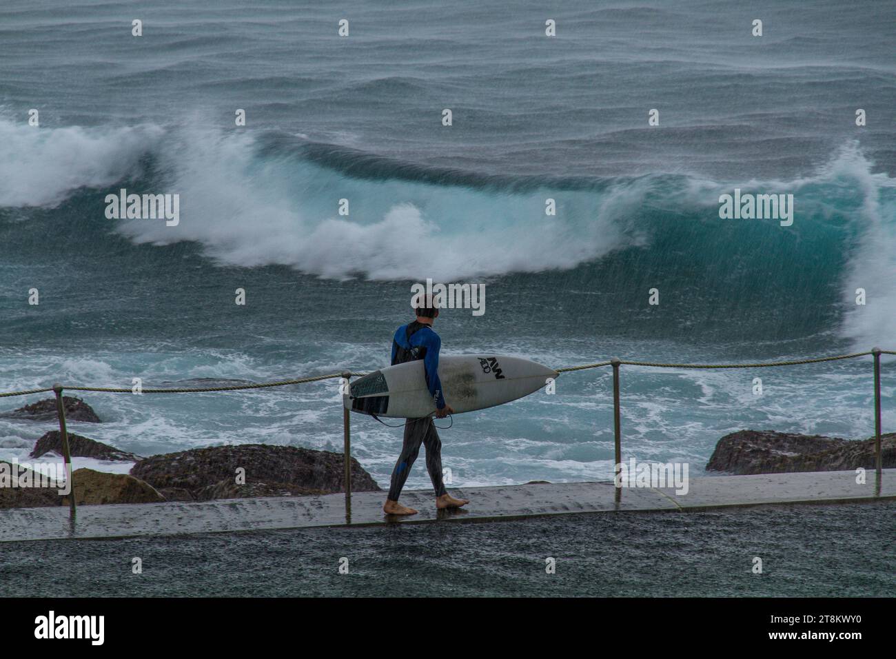 A young surfer walks on the edge of Bronte ocean pool contemplating entering the water during a storm. Stock Photo