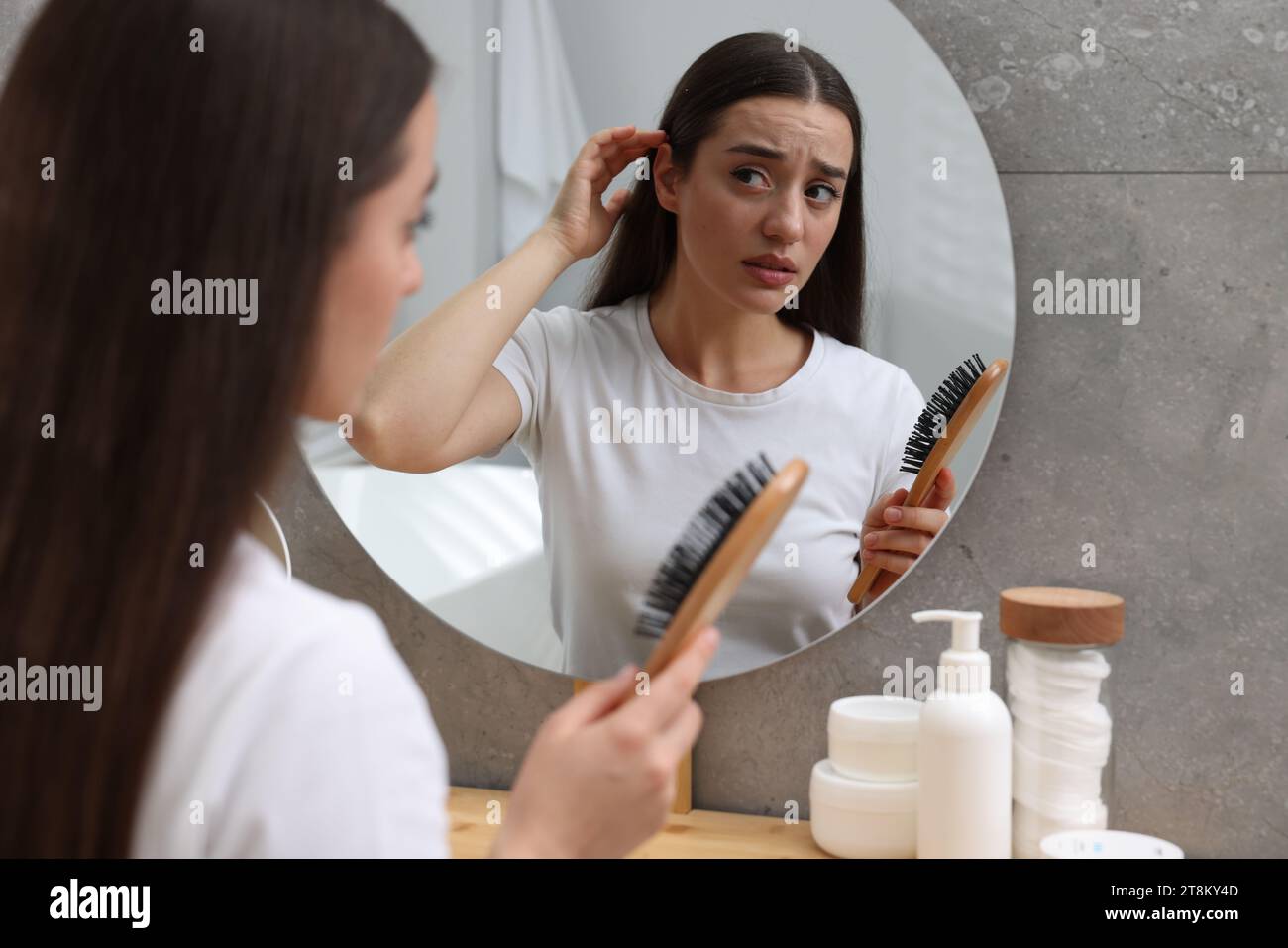 Emotional woman with brush suffering from dandruff near mirror at home. Stock Photo