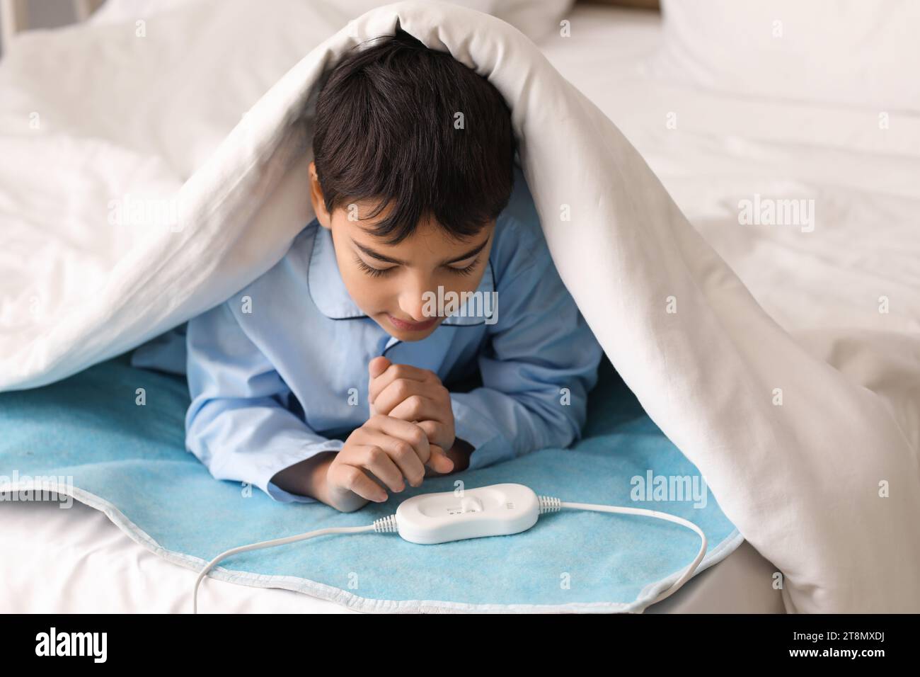 Little boy lying under blanket on electric heating pad in bedroom Stock