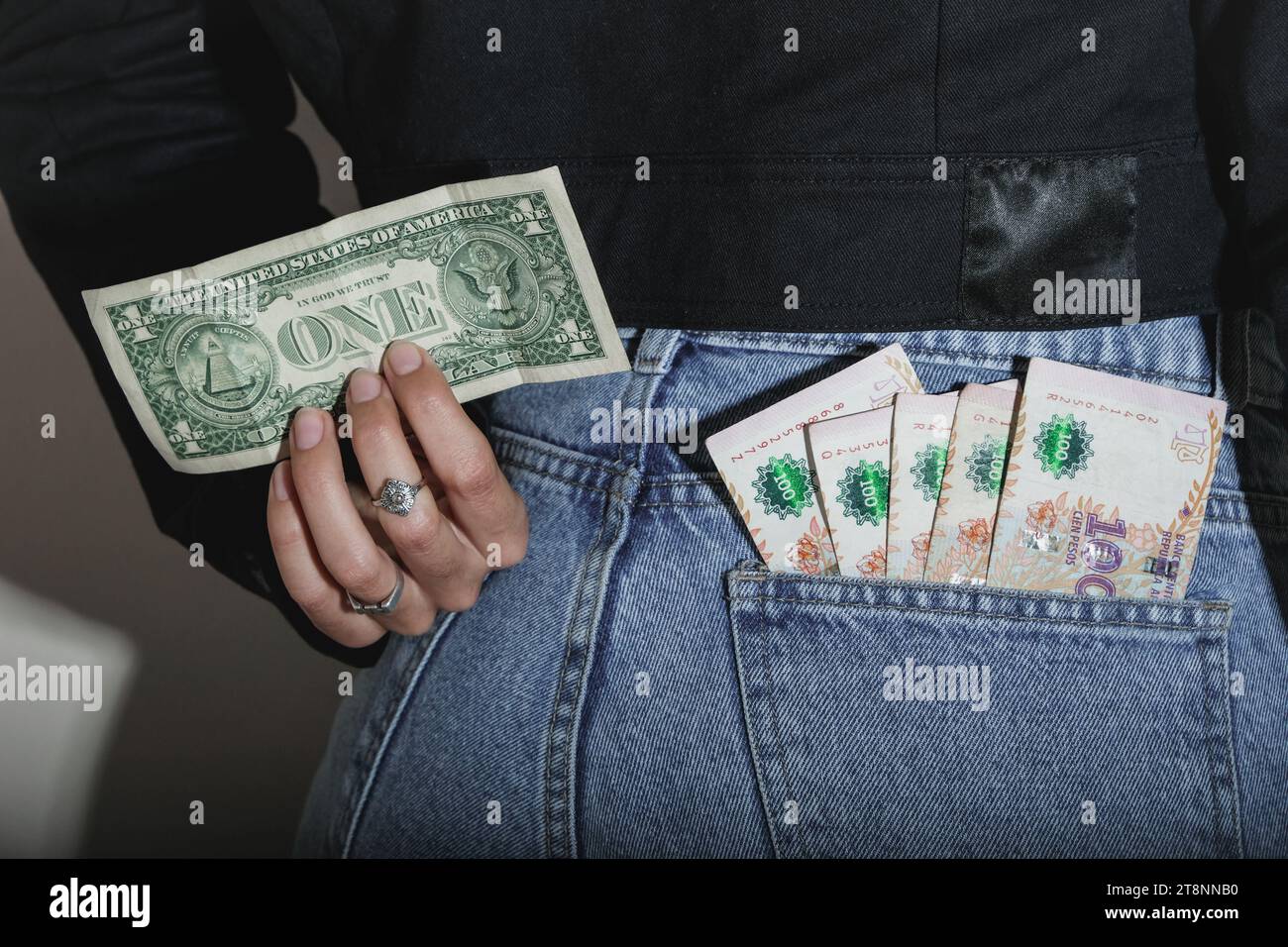 Woman Holding A One Dollar Bill And A Stack Of Argentine Pesos Inside A Jeans Pocket. Financial concept related to inflation and economic crisis. Stock Photo