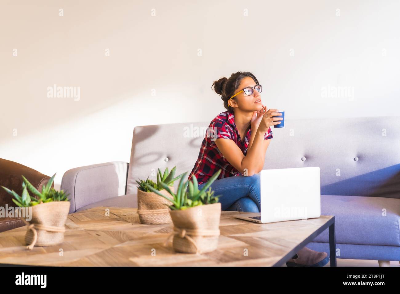 Horizontal photo of a young woman drinking coffee while working at home Stock Photo