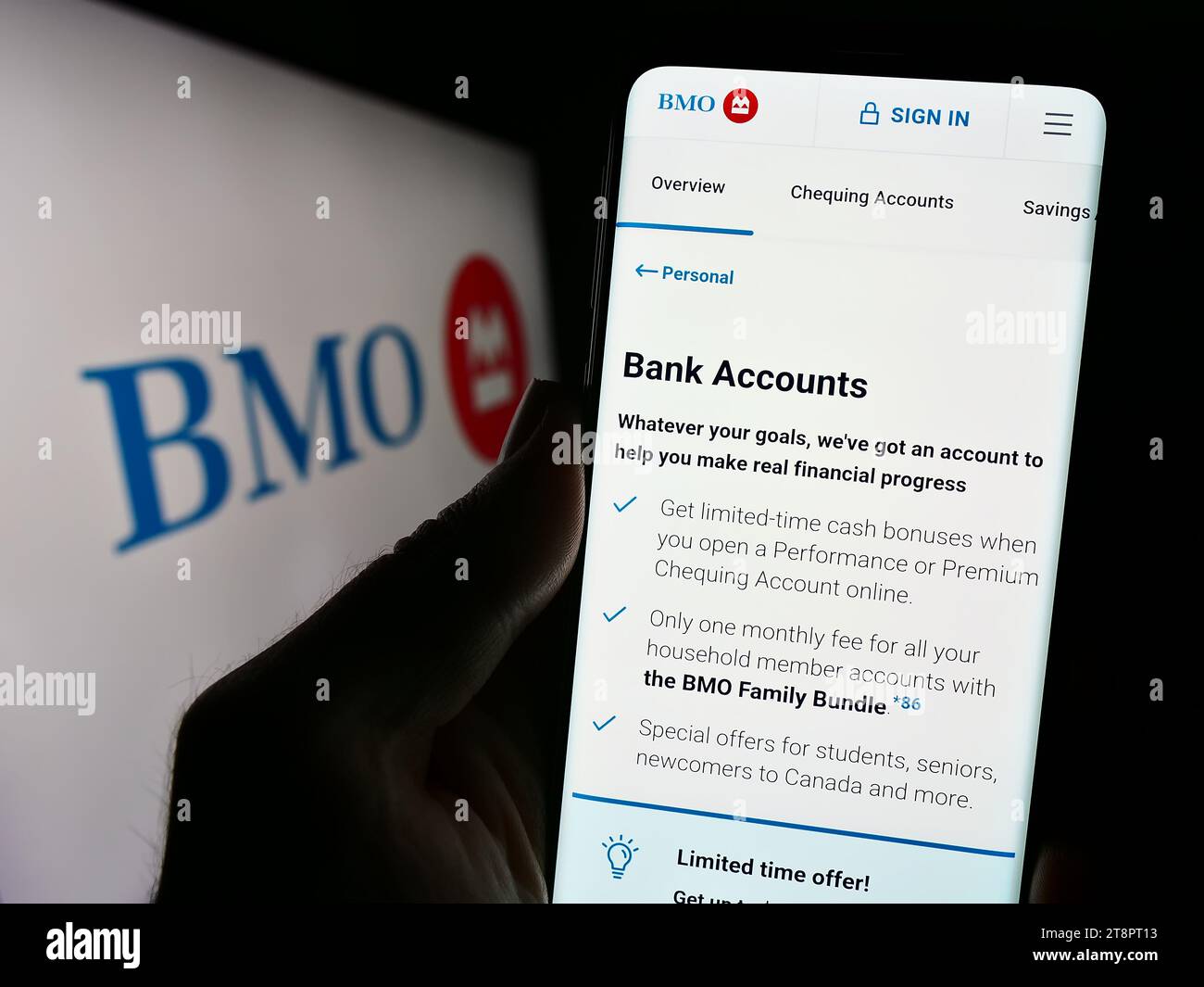 Person holding mobile phone with website of Canadian financial company Bank of Montreal (BMO) with logo. Focus on center of phone display. Stock Photo