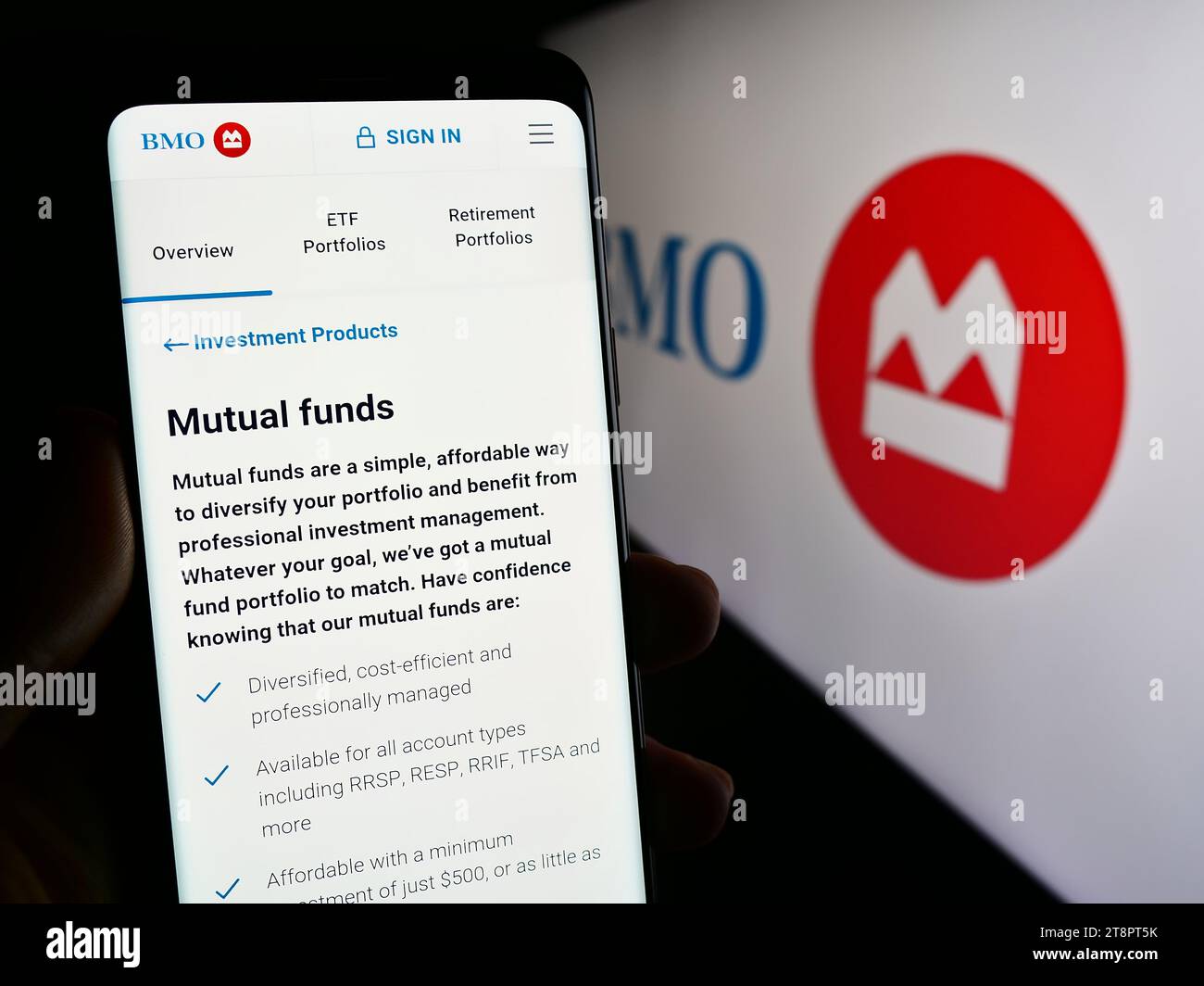 Person holding smartphone with webpage of Canadian financial services company Bank of Montreal (BMO) with logo. Focus on center of phone display. Stock Photo