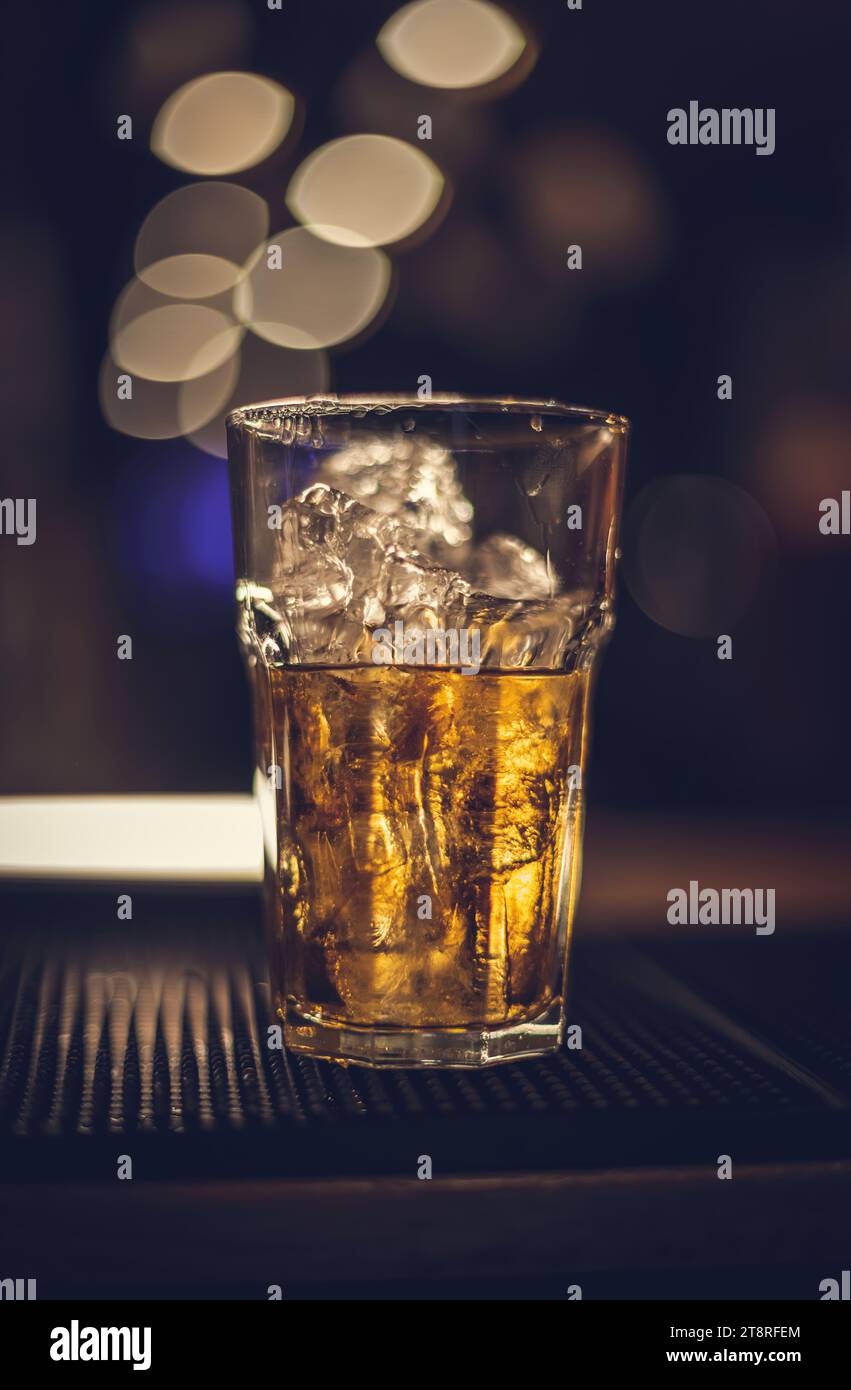 Glass of whiskey on the ice rocks placed on a black bar mat Stock Photo