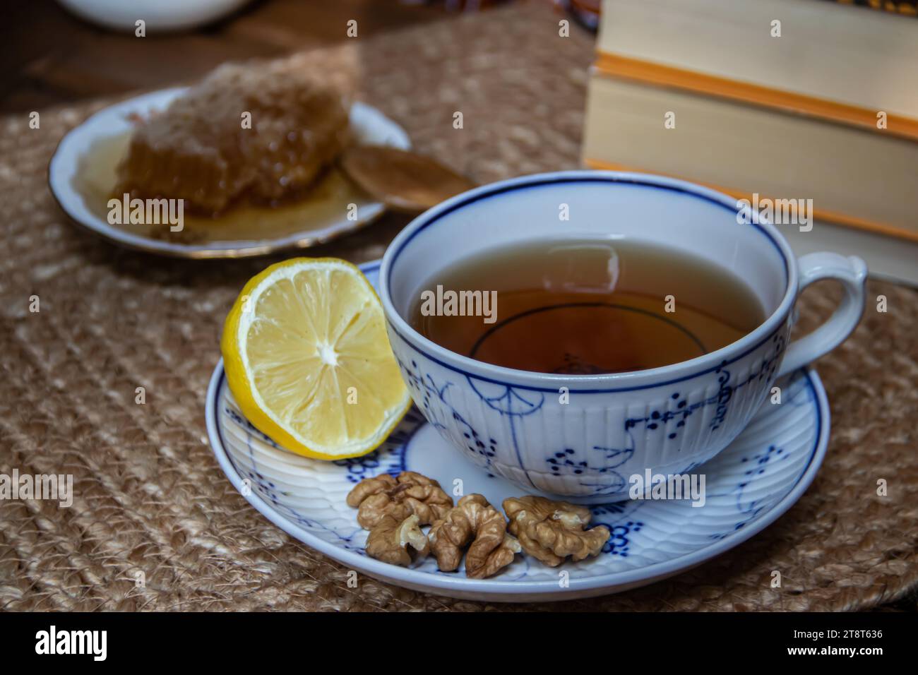 Morning setup on wooden table at balcony, books to read, cup of natural tea, teapot, organic honey from farm, fresh green tea leaves and organic fruit Stock Photo