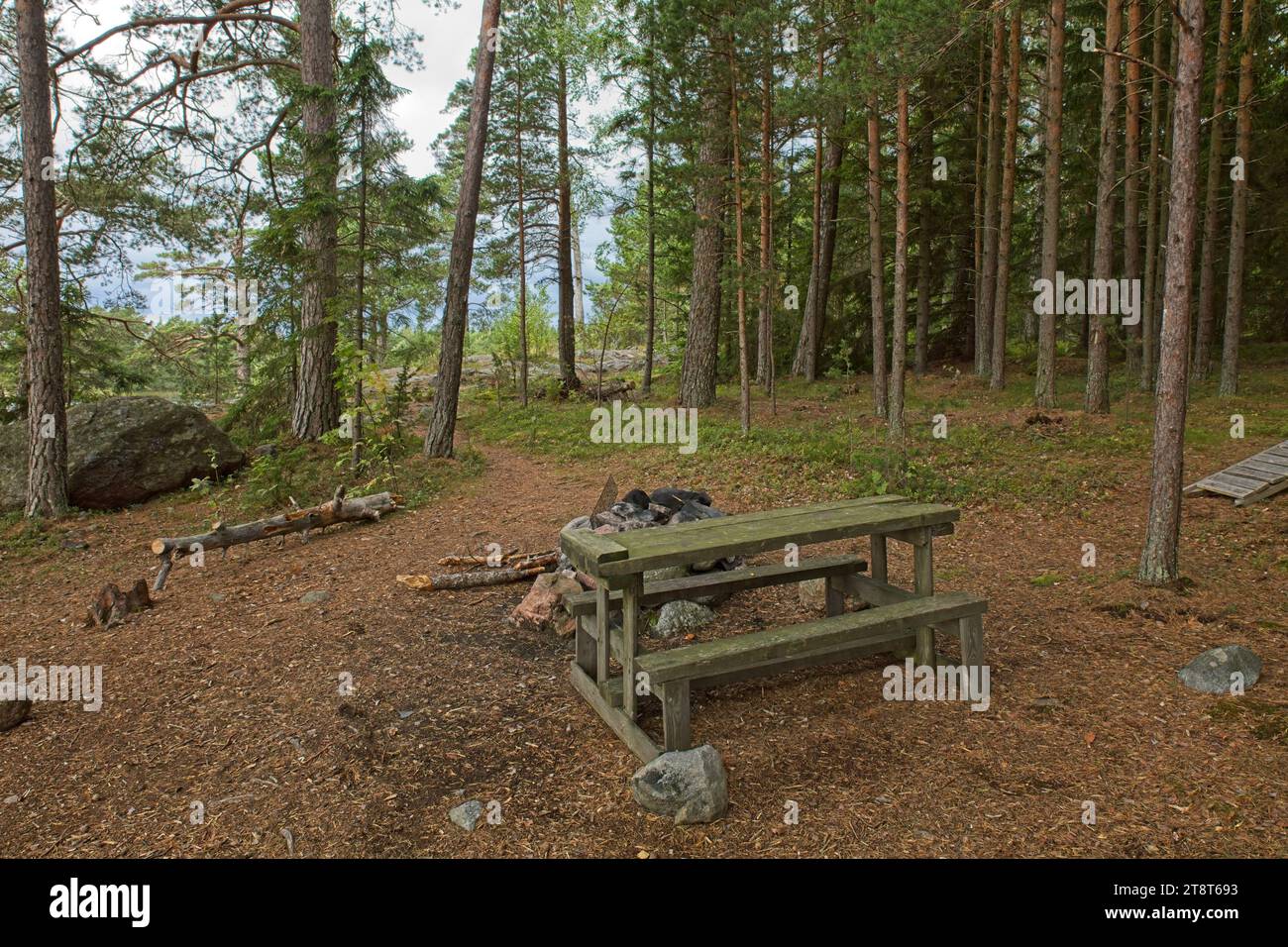 Camping fire behind table and benches on the island of Linlo in forest, Kirkkonummi, Finland. Stock Photo