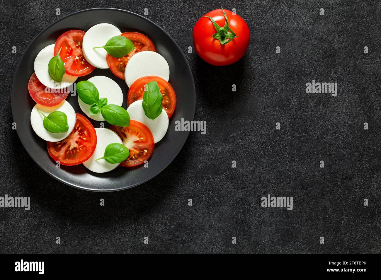 Caprese, Italian antipasto, and whole tomato, on dark background, top view, space to copy text. Stock Photo