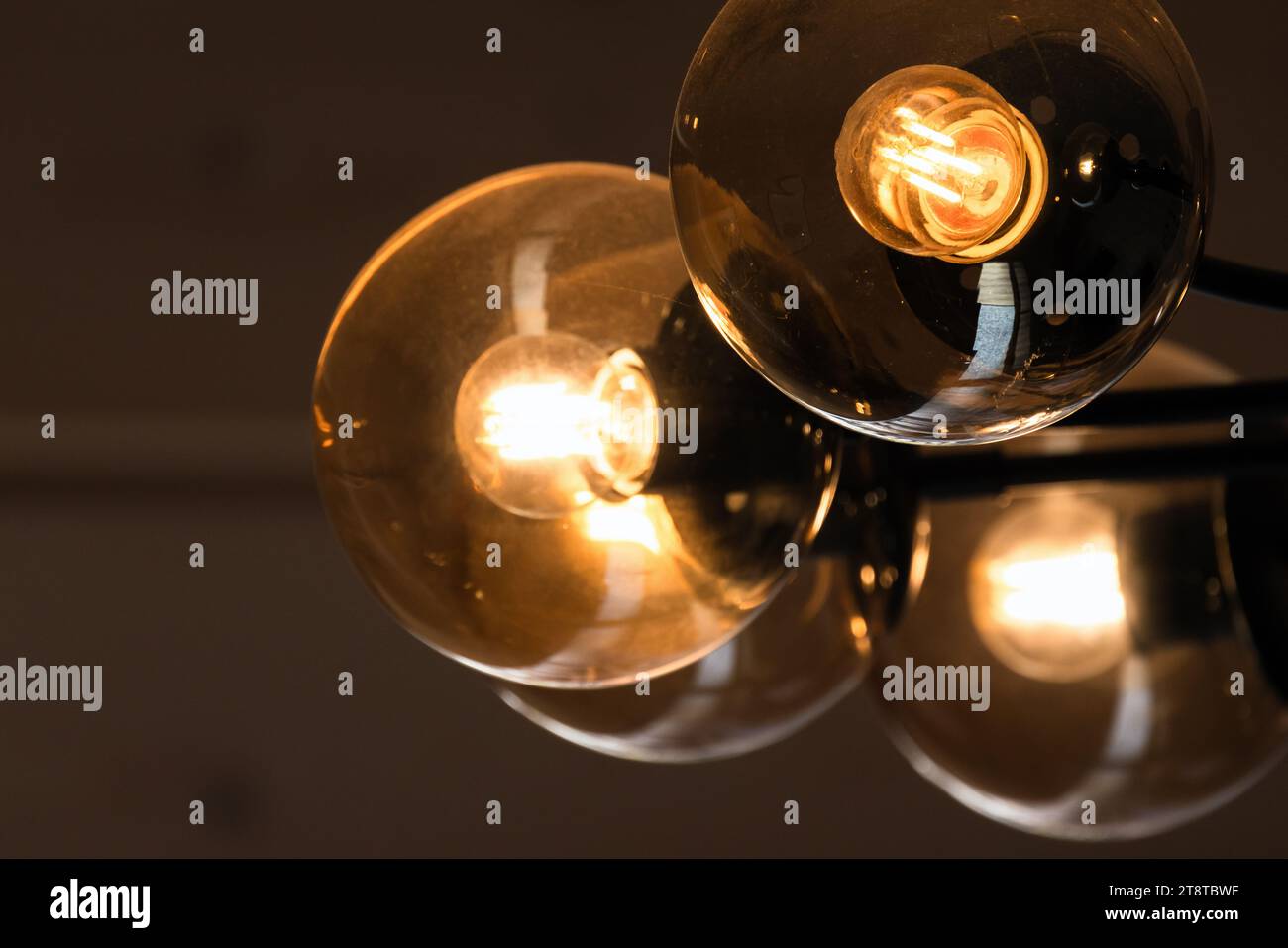 Tungsten lamps glow in round glass lampshades, modern chandelier close-up view Stock Photo