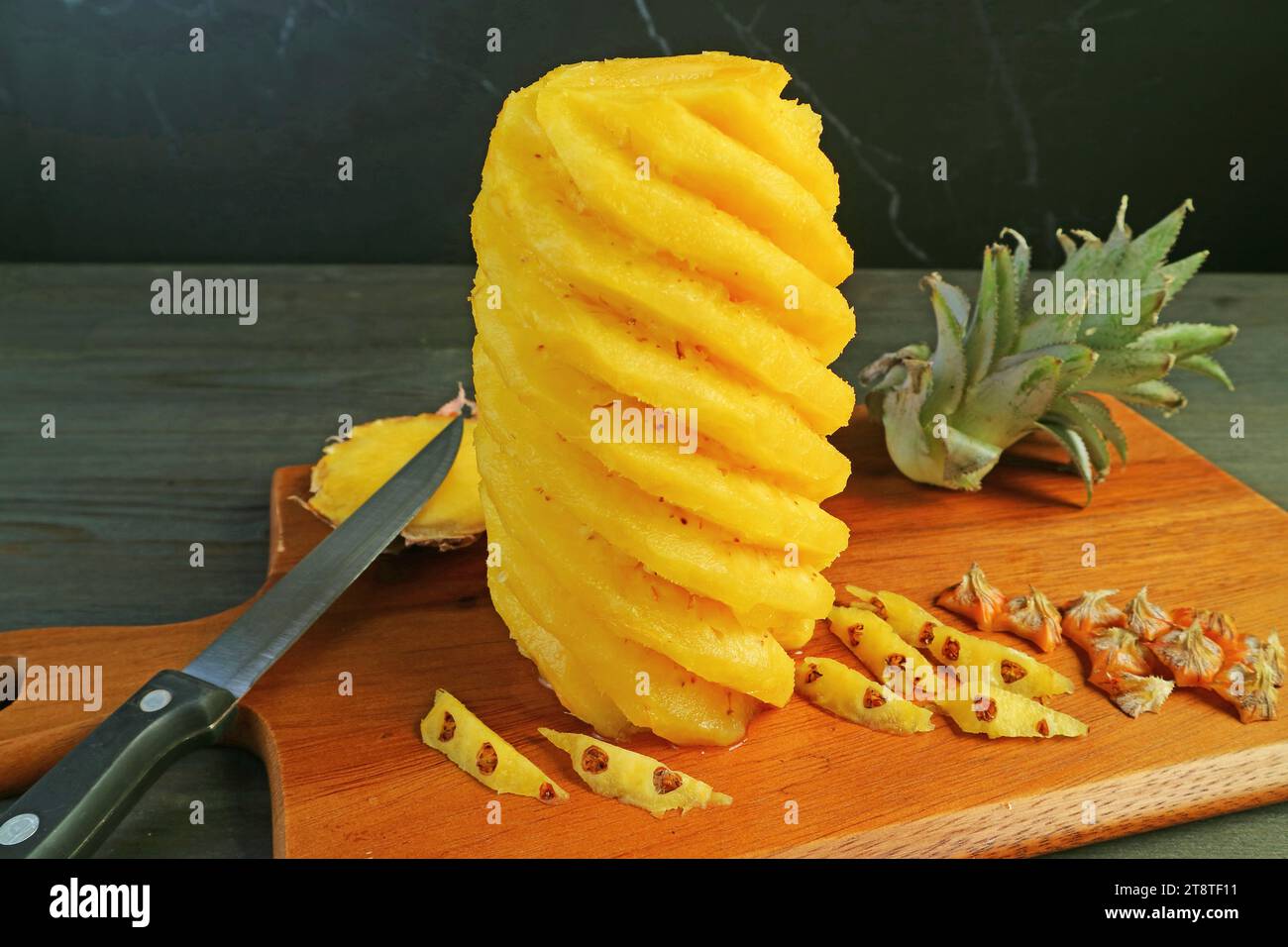 Peeled and cut fresh ripe pineapple on wooden cutting board Stock Photo