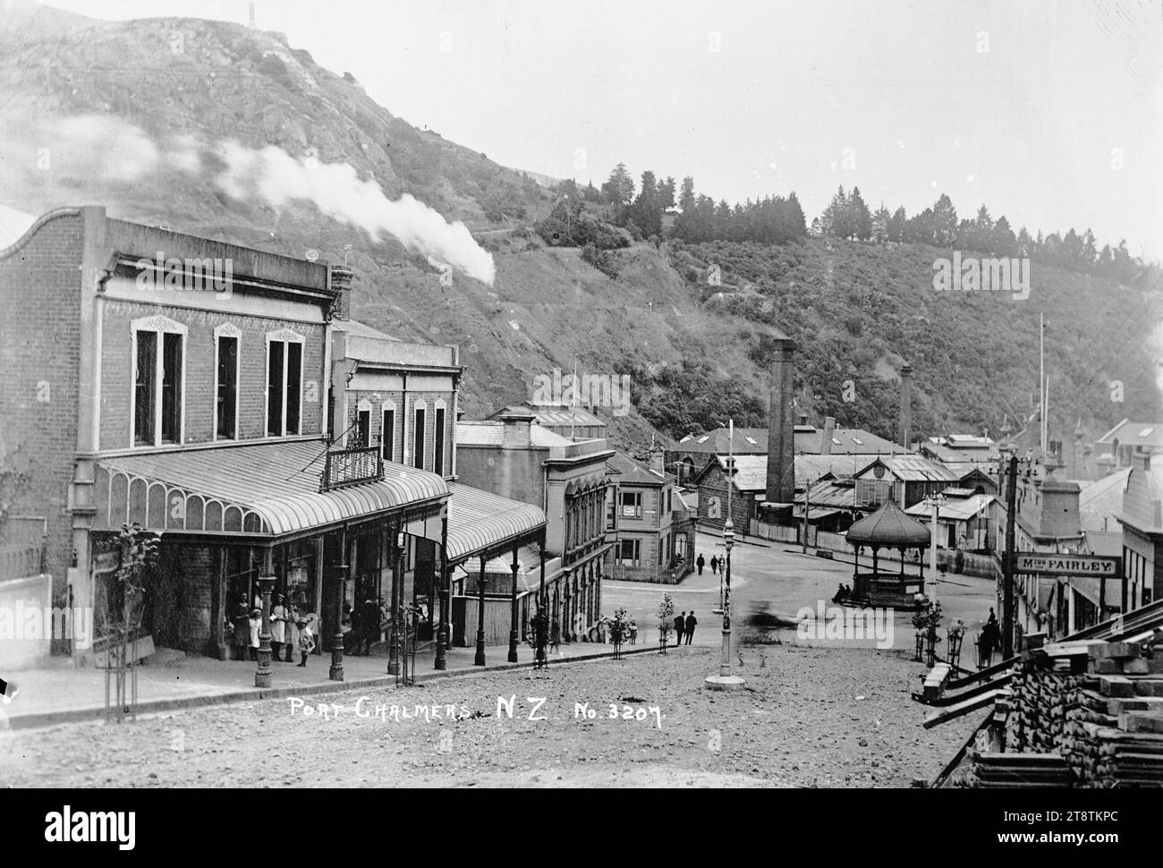 View of Port Chalmers township, View of Port Chalmers township looking down Grey Street towards the band rotunda at the junction of George, Grey and Beach Streets. Commercial buildings line both sides of the street, and there is smoke coming from a tall factory chimney to the left of the band rotunda. The premises of McEwan's (boot makers) are on the left, and Miss Fairley's (refreshment rooms) are on the right. in the early 1900s Stock Photo