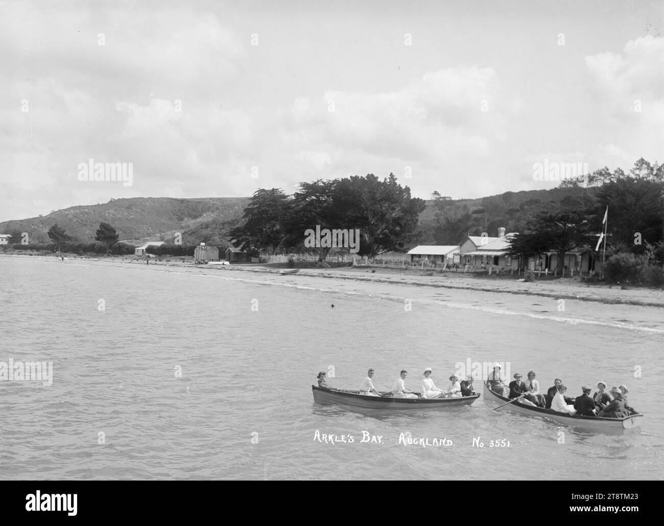 Row boats at Arkles Bay, Auckland, New Zealand, Two boat loads of people rowing in Arkles Bay in front of Arkle's Bay House. Kia Ora House can be seen in the distance on the far right. A flagpole is on the right of Arkle's Bay House, in early 1900s (possibly from the jetty at the north end of the bay Stock Photo