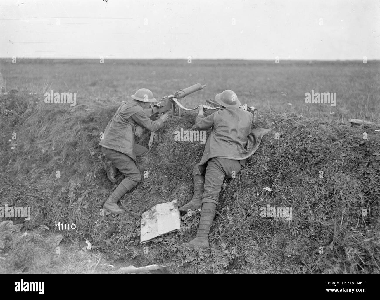 New Zealand troops using a German machine gun, Beaudignies, World War I, Two New Zealand soldiers firing a captured German machine gun at Beaudignies during World War I. One soldier is sighting and firing the gun while another is holding the ammunition belt. Both are resting against a trench wall with the machine gun on the top of it. Photograph taken 3 November 1918 Stock Photo