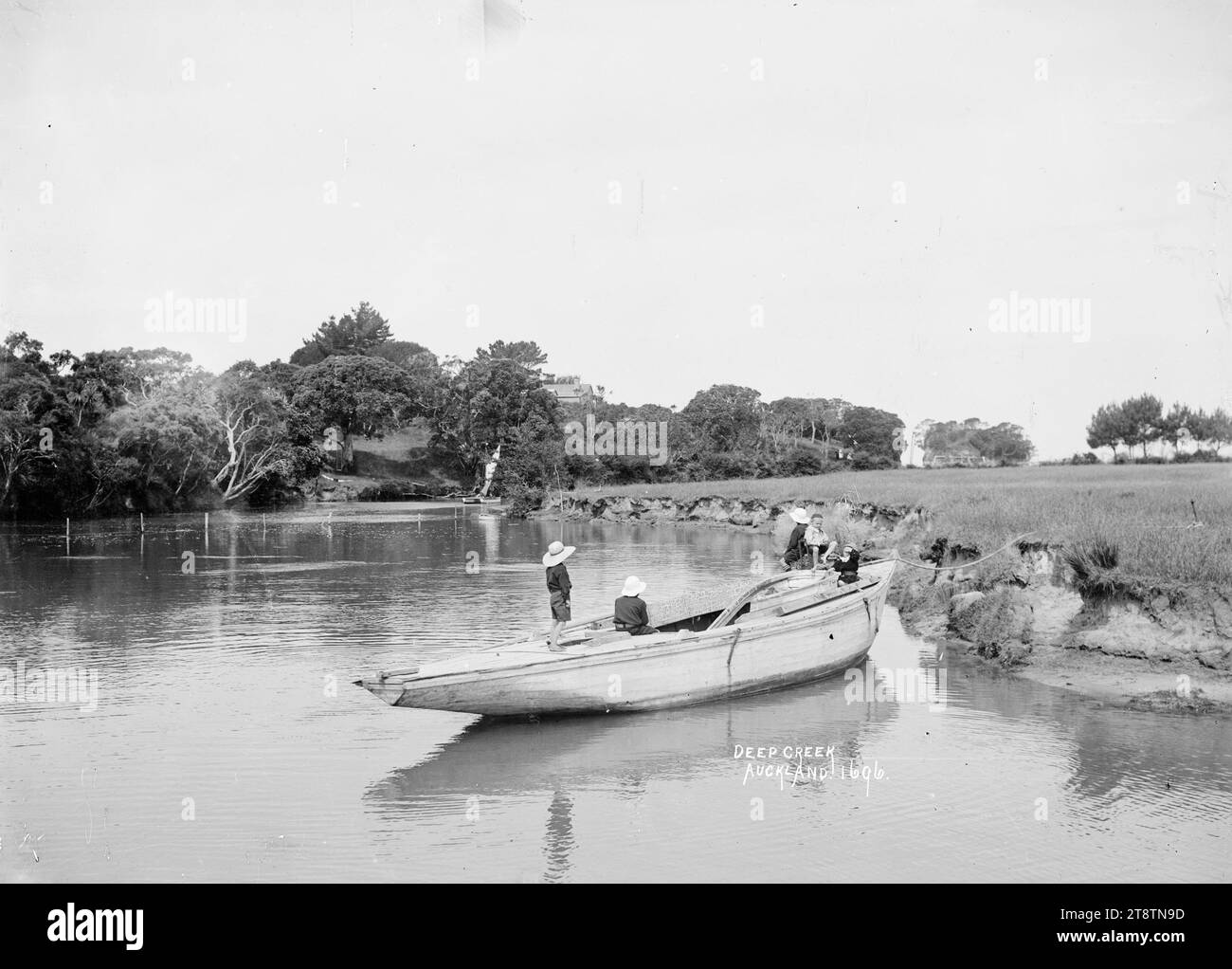 Boys playing on a boat at Deep Creek, Torbay, Auckland, New Zealand, Boys playing on an old yacht tied up to the bank at Deep Creek. A catamaran can be seen in the distance. Taken in the early 1900s Stock Photo