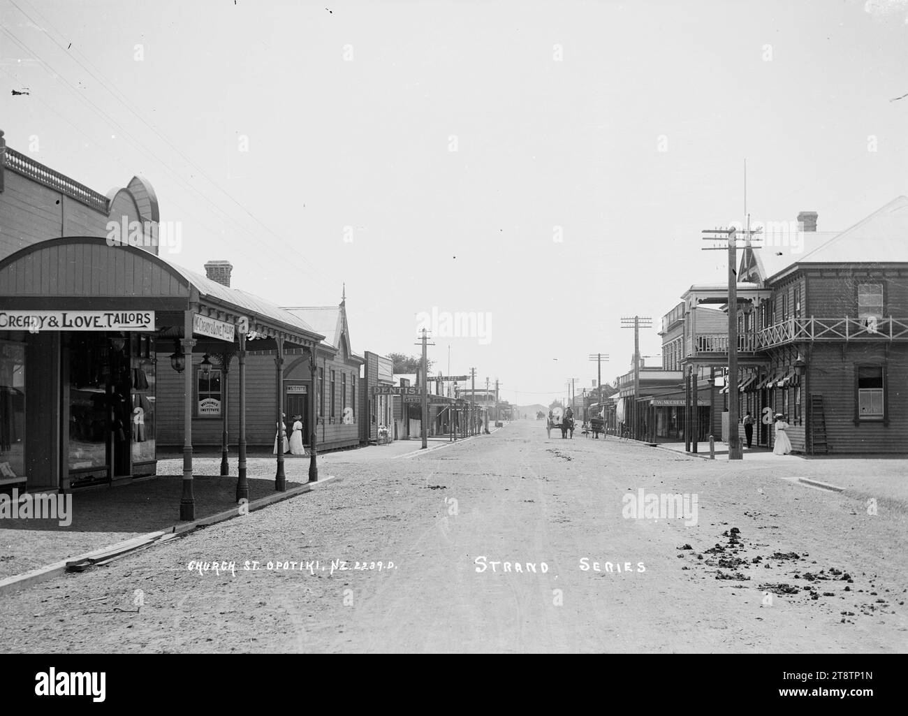 Church Street, Opotiki, View looking down Church Street (now known as Elliot Street) with the Royal Hotel on the right; McCready & Love (tailors), Mechanics Institute; dentist, saddler, and other businesses on the left. The Masonic Hotel can be seen in the far distance on the left. Two women are standing at the entrance to the Mechanics Institute; a pram is on the footpath outside the dentist; a horse and cart are heading towards the photographer in early 1900s Stock Photo