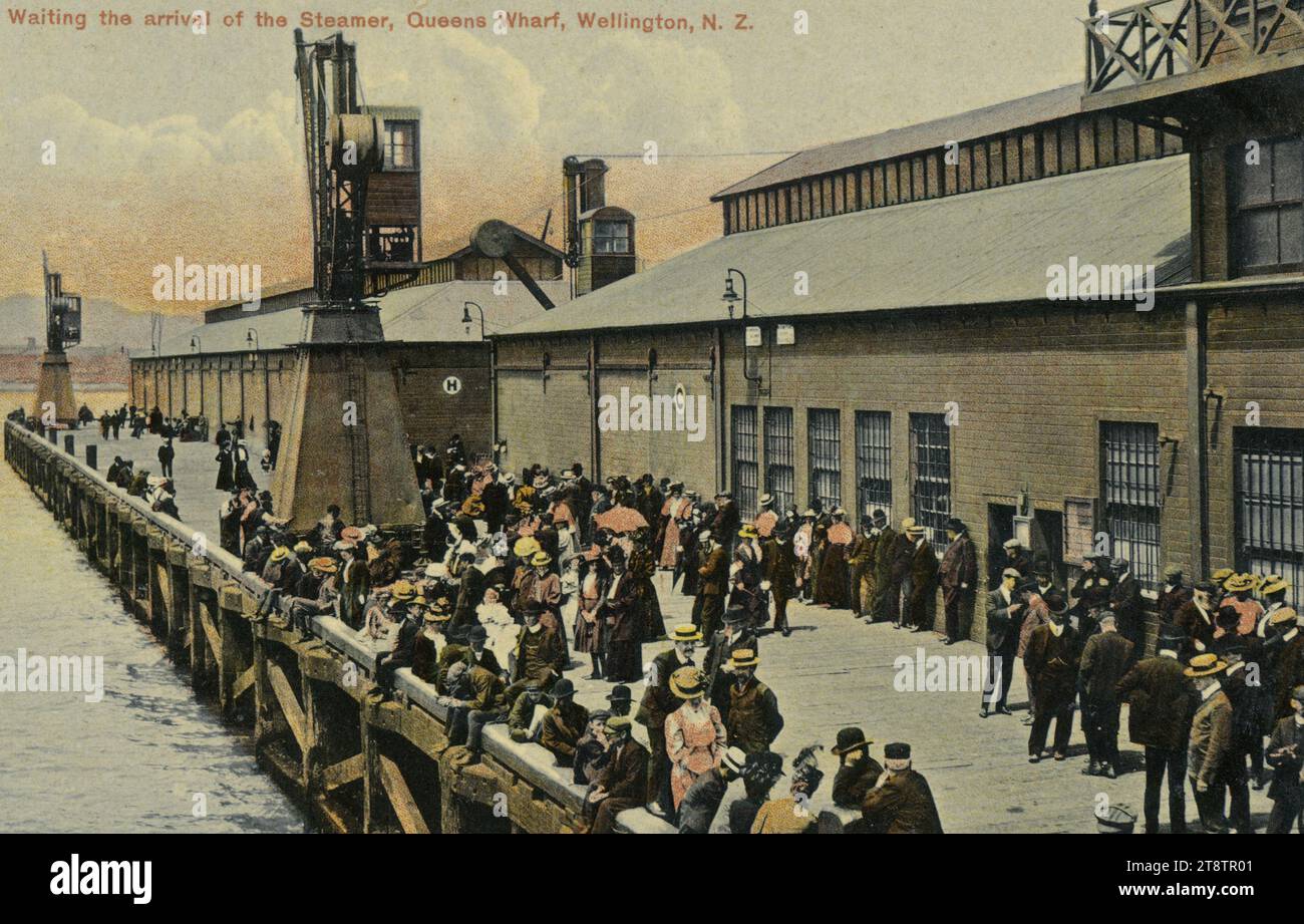 Postcard. Waiting the arrival of the steamer, Queens Wharf, Wellington, New Zealand, N.Z. Industria series. Fergusson Limited, Sydney and London. No. 1007. ca 1905-1914?, Shows a crowd of men and women waiting on the wharf beside the sheds and buildings. Boaters and bowler hats, and parasols, can be seen in the crowd Stock Photo